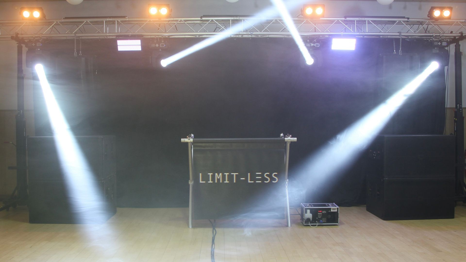 Stage setup with bright spotlights illuminating a backdrop with the text 'LIMIT-LESS'.