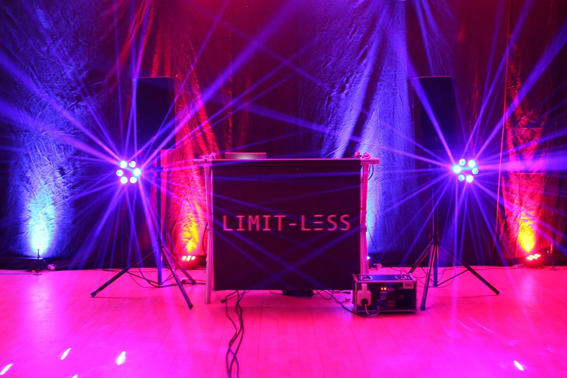 DJ booth with the word 'Limit-Less' under colorful stage lights and speakers.