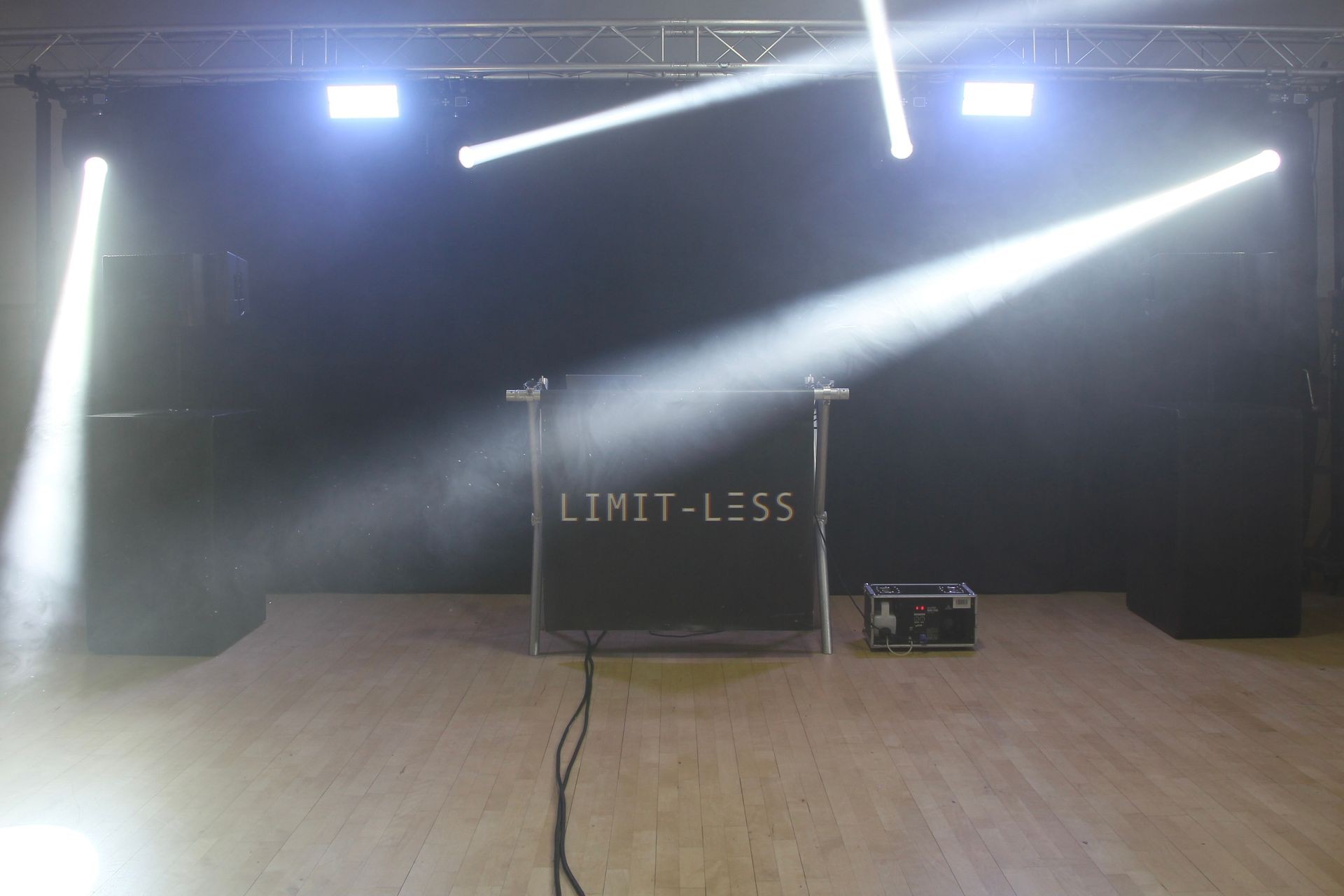 Stage setup with speakers, light beams, and 'LIMIT-LESS' sign.