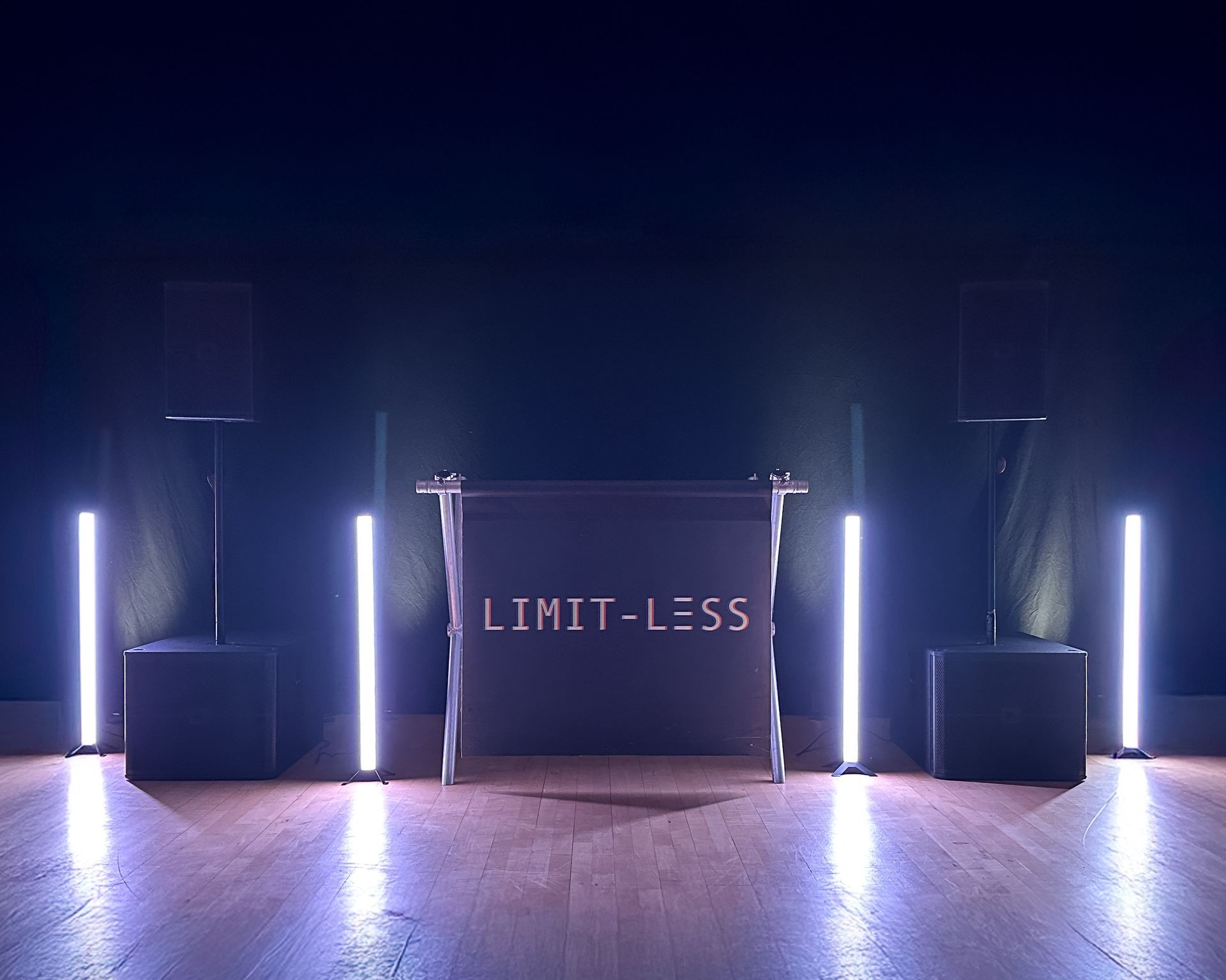 Minimalist DJ setup with glowing lights and 'LIMIT-LESS' sign in dark room.