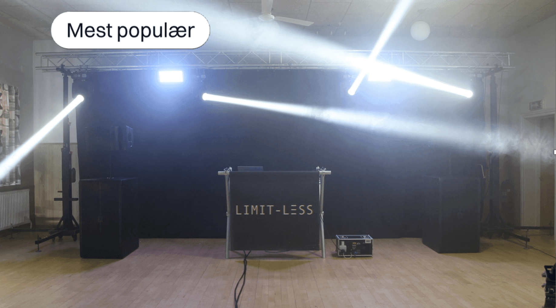 DJ booth with 'LIMIT-LESS' sign and lights in a dim room with wooden floor.