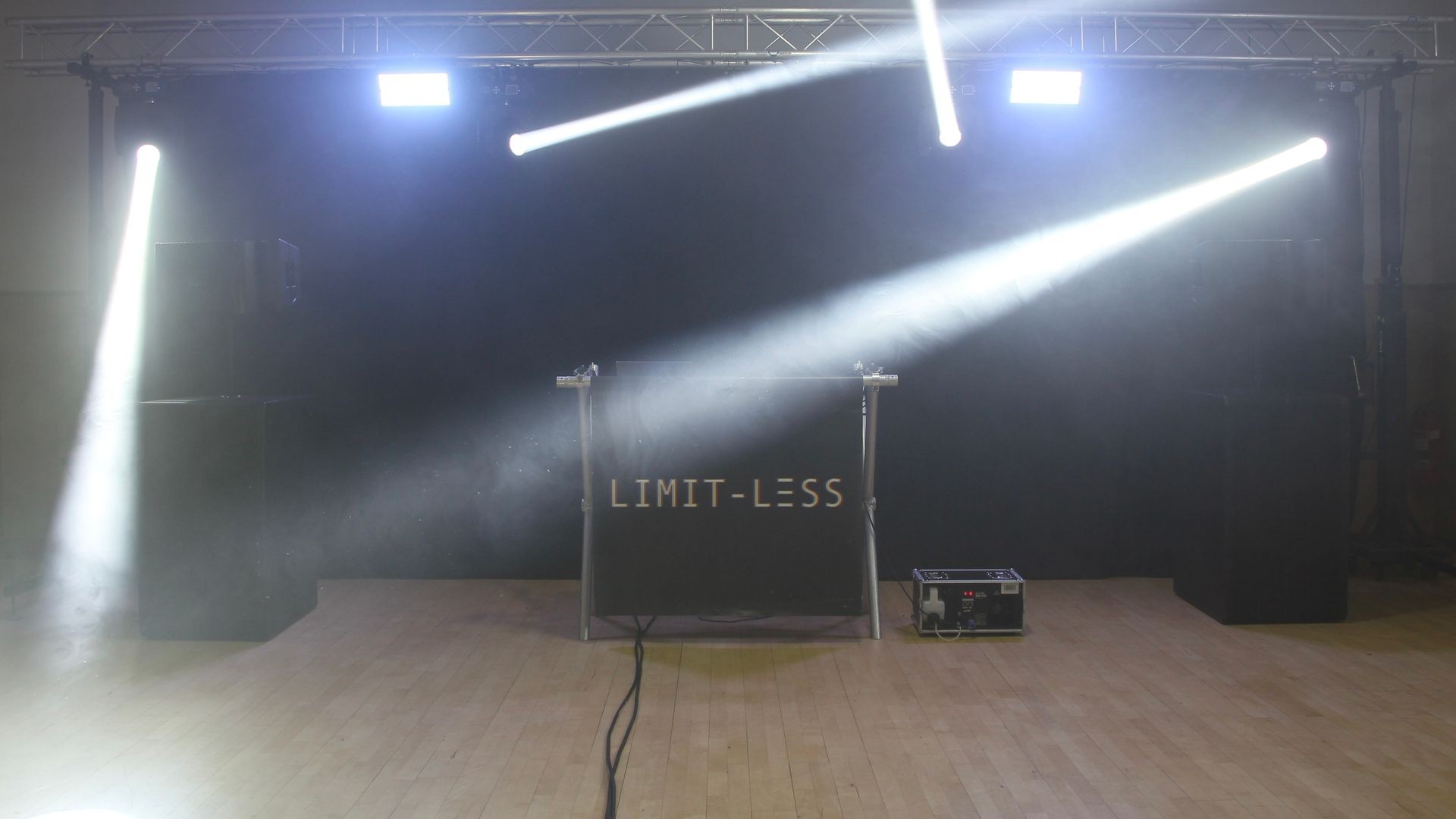 Stage with bright spotlights and a setup labeled 'Limit-less' on a wooden floor.