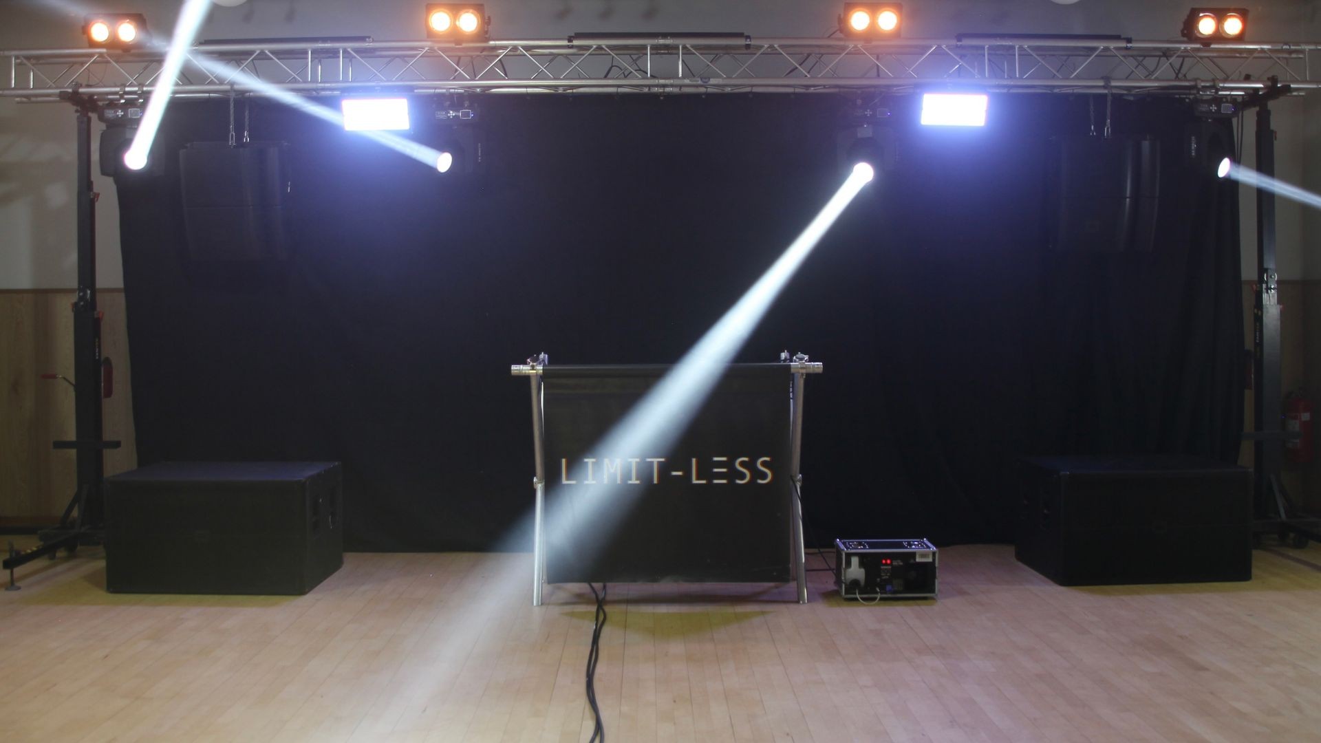 Stage setup with spotlights and 'LIMIT-LESS' sign in a dimly lit venue.