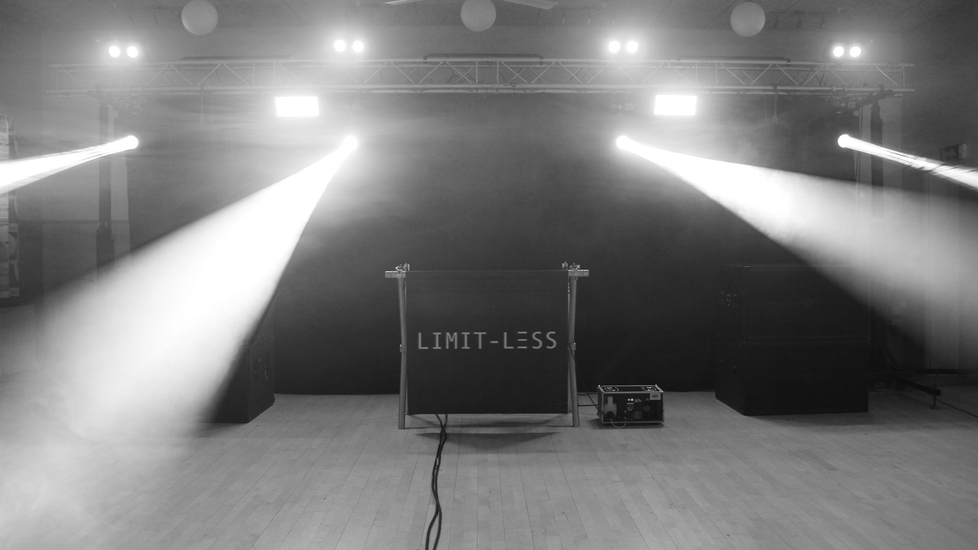 Stage with intense spotlights and a sign reading LIMIT-LESS in a dark room.